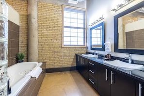 Ein modernes Badezimmer mit Backsteinwand, großem Fenster, Badewanne und Waschtisch mit zwei Becken.