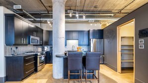 Une cuisine moderne avec des meubles de couleur sombre, un îlot central doté de tabourets de bar, des appareils en acier inoxydable et des conduits apparents au plafond.