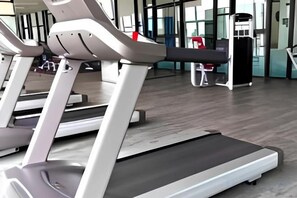 Una caminadora en un gimnasio con piso de madera y equipo de ejercicio al fondo.