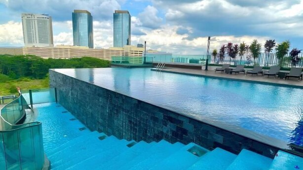 A rooftop infinity pool with a city skyline in the background. - City View Southkey 2BR 2FREE 18F By Natol (Plentong)