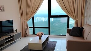 A modern living room with a flat-screen TV, a coffee table, and a sofa. - City View Southkey 2BR 2FREE 18F By Natol (Plentong)