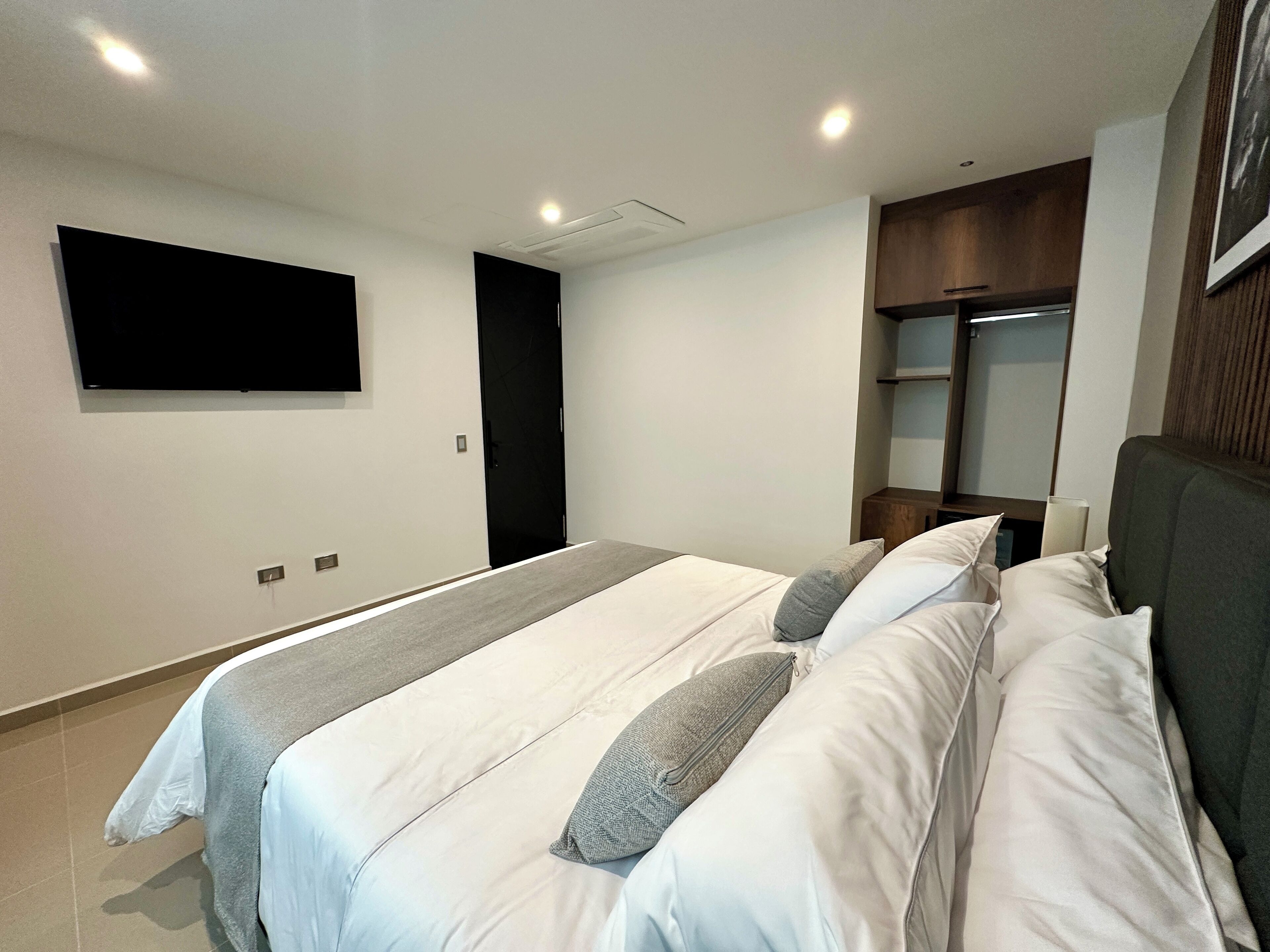 Una camera da letto moderna con un letto grande, una televisione a schermo piatto montata a parete e un'armadio in legno.