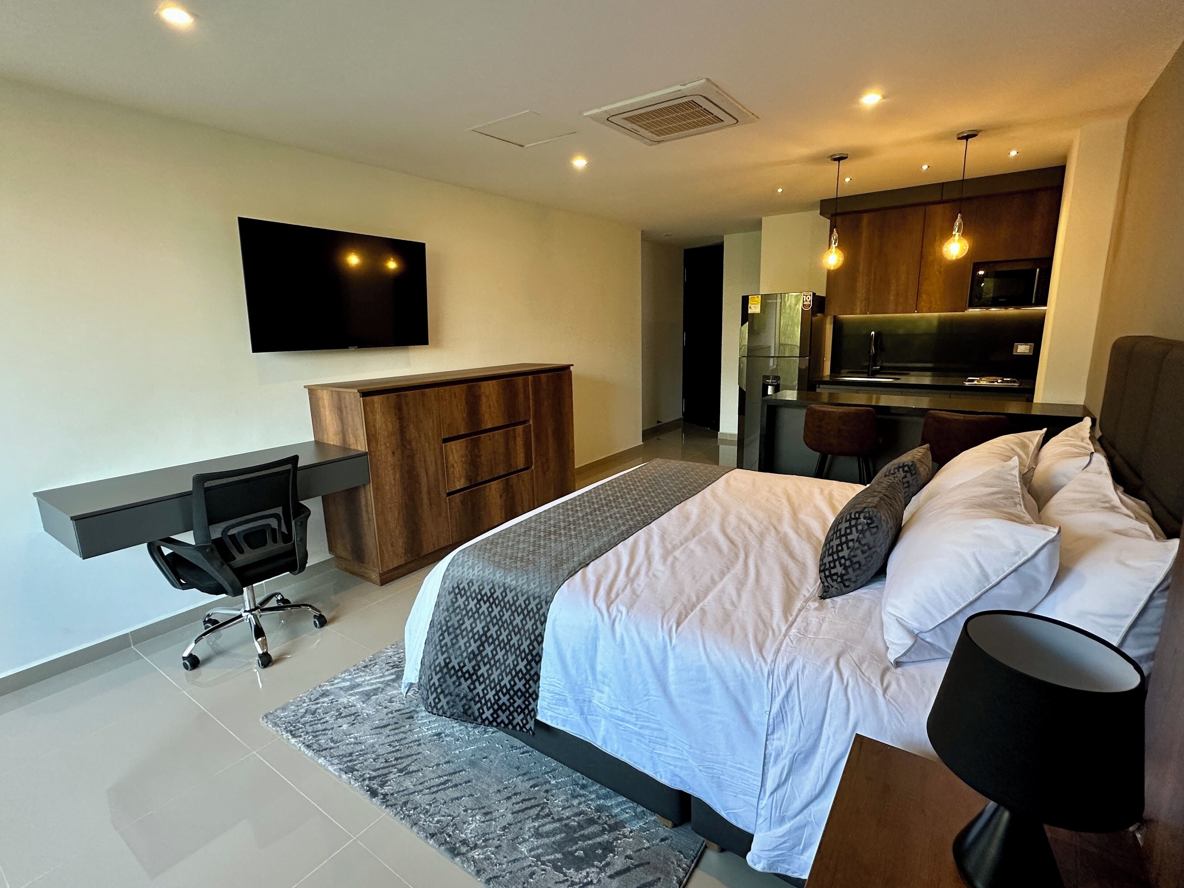 A modern bedroom with a bed, desk, and kitchenette.