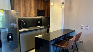 Cozinha moderna com frigorífico, micro-ondas e pia. Possui duas banquetas de bar e luminárias pendentes.