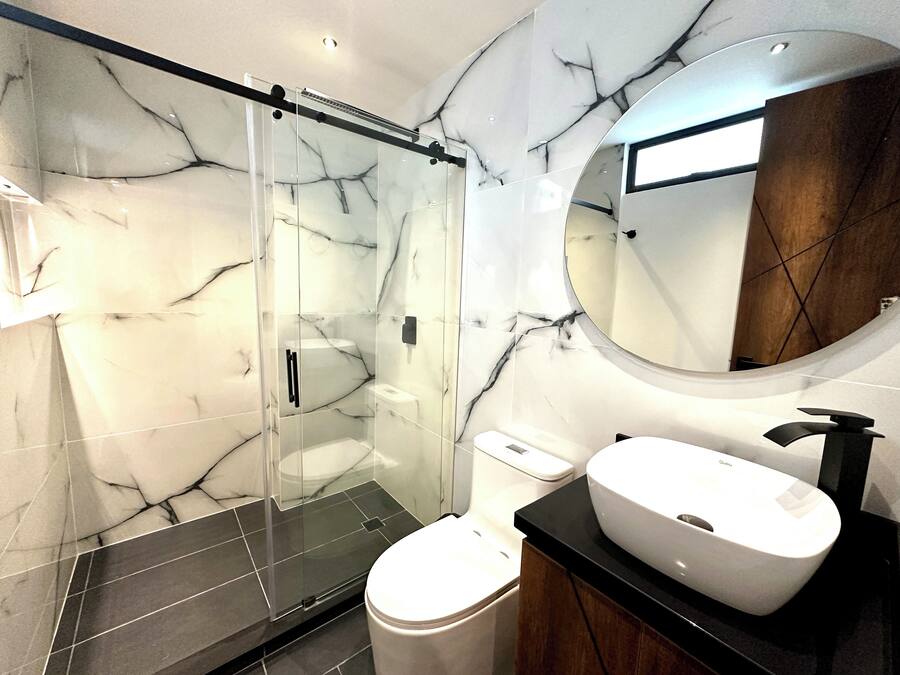 Un baño moderno con ducha envuelta en vidrio, inodoro y lavamanos con espejo superior.