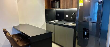 Una cocina moderna con un refrigerador negro, un microondas y un lavamanos. Hay dos lámparas colgantes y un taburete de bar.