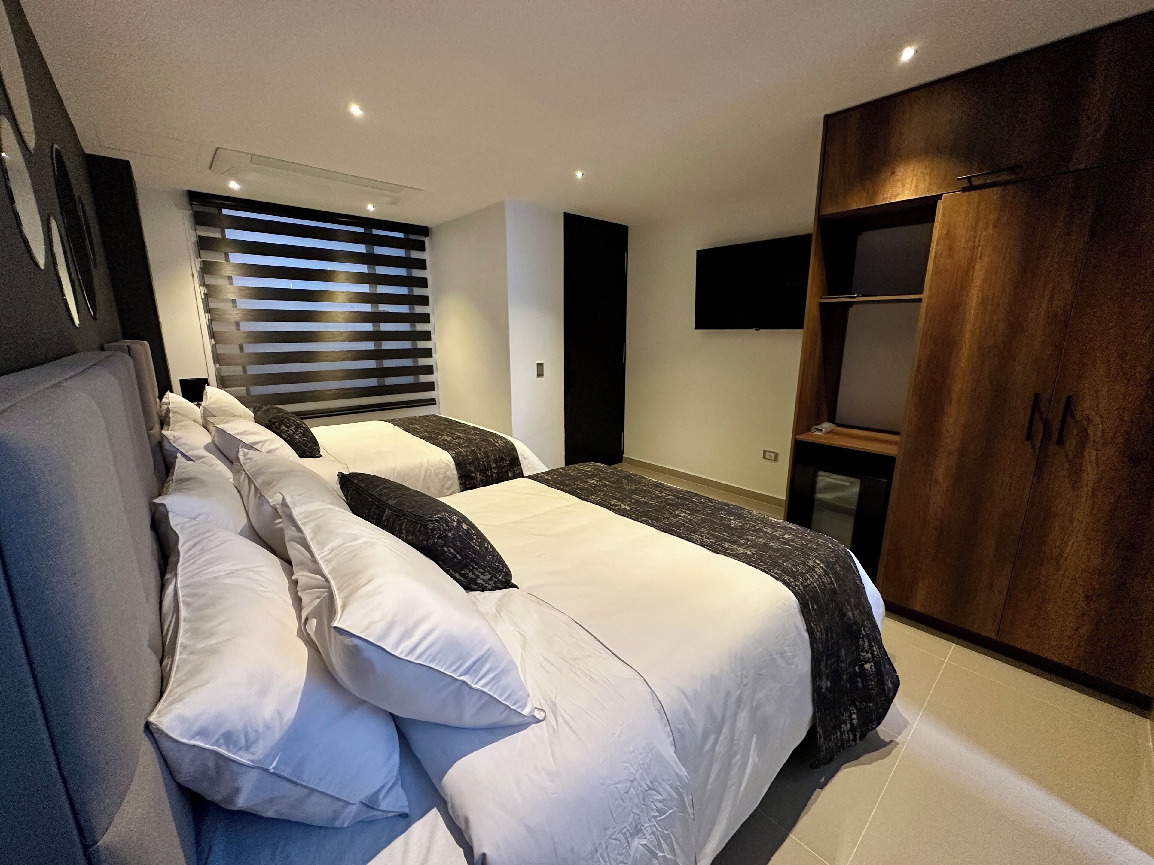 A modern hotel room with a large bed, a wardrobe, and a TV mounted on the wall.