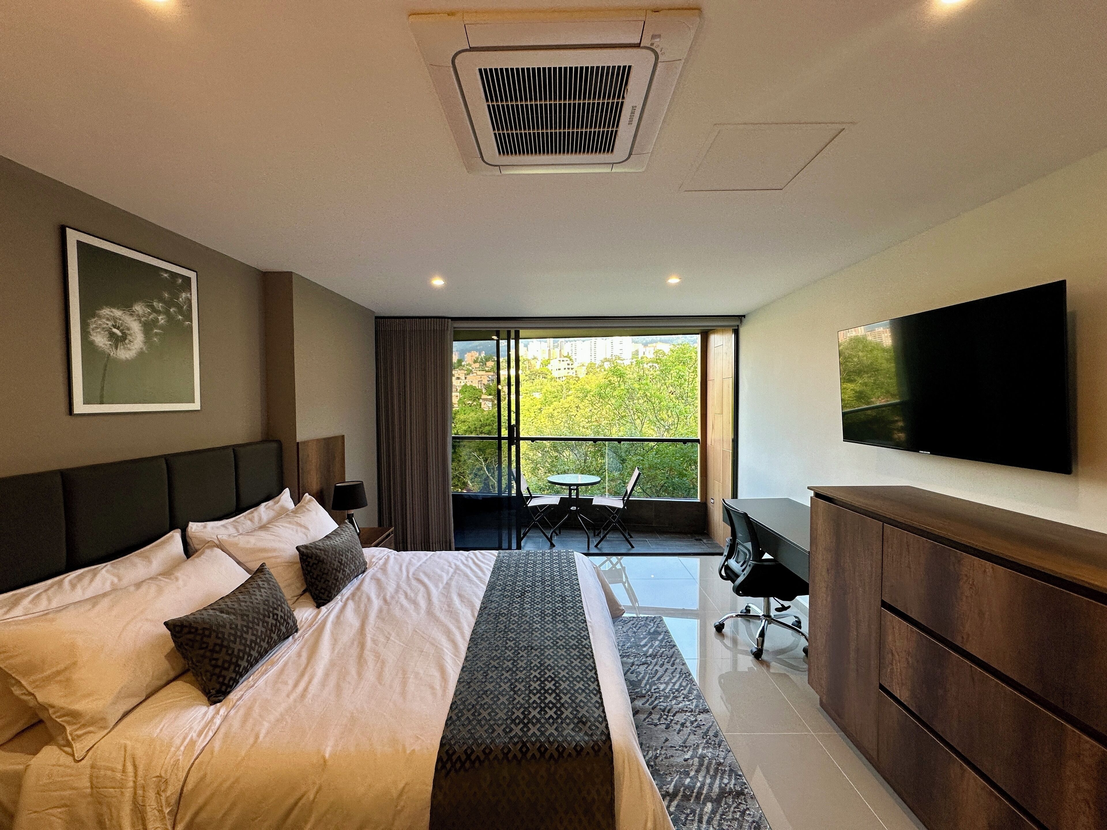 Quarto de hotel moderno com uma cama grande, uma escrivaninha, uma cadeira, uma TV e uma varanda com vista para a cidade.