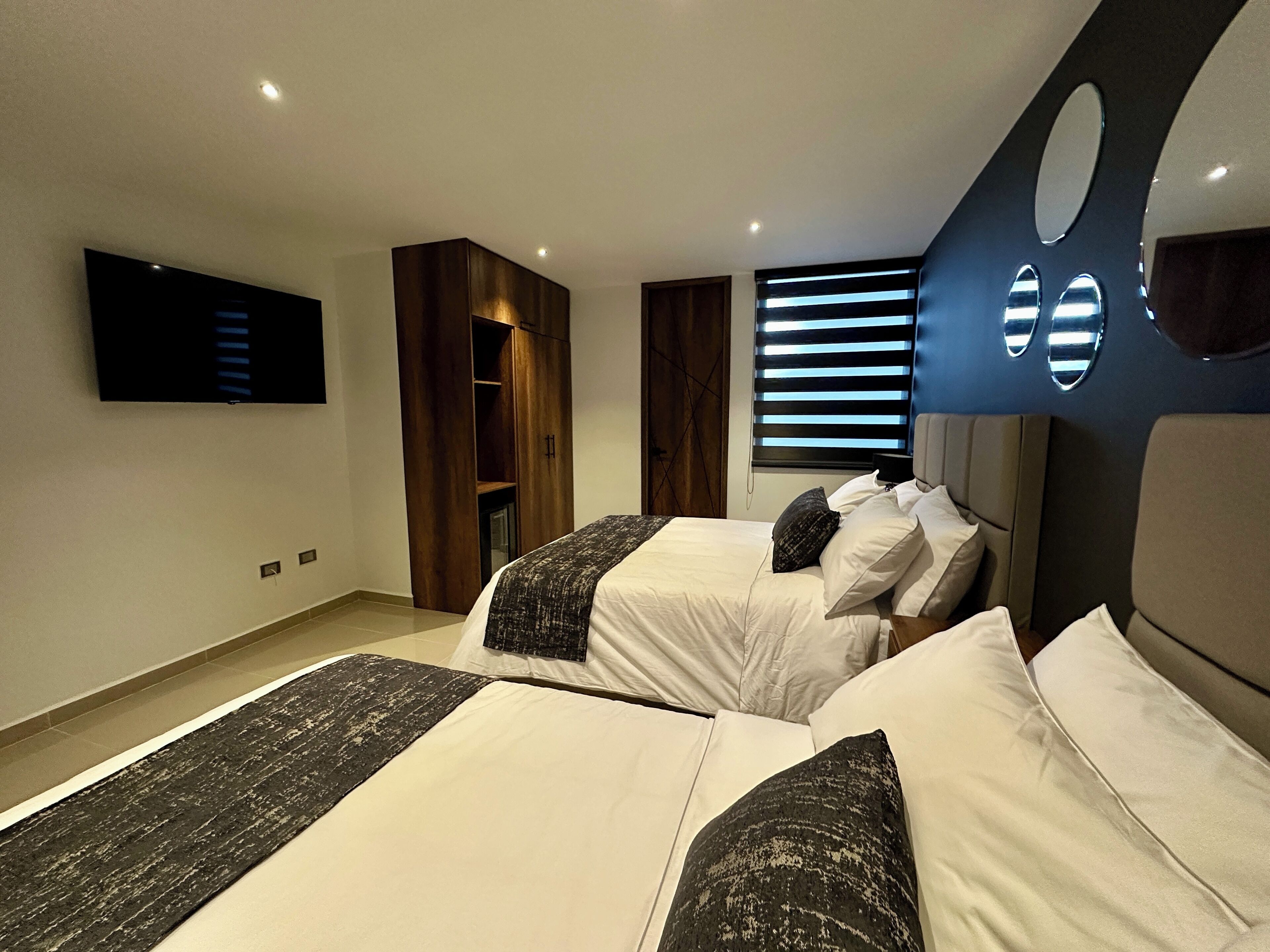Een moderne slaapkamer met twee bedden, een televisie, een ingebouwde kast en een raam met zonwering.