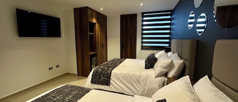 A modern bedroom with two beds, a TV, built-in wardrobe, and a window with blinds.