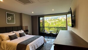 Quarto de hotel com uma cama grande, uma escrivaninha e uma varanda com vista para a cidade.