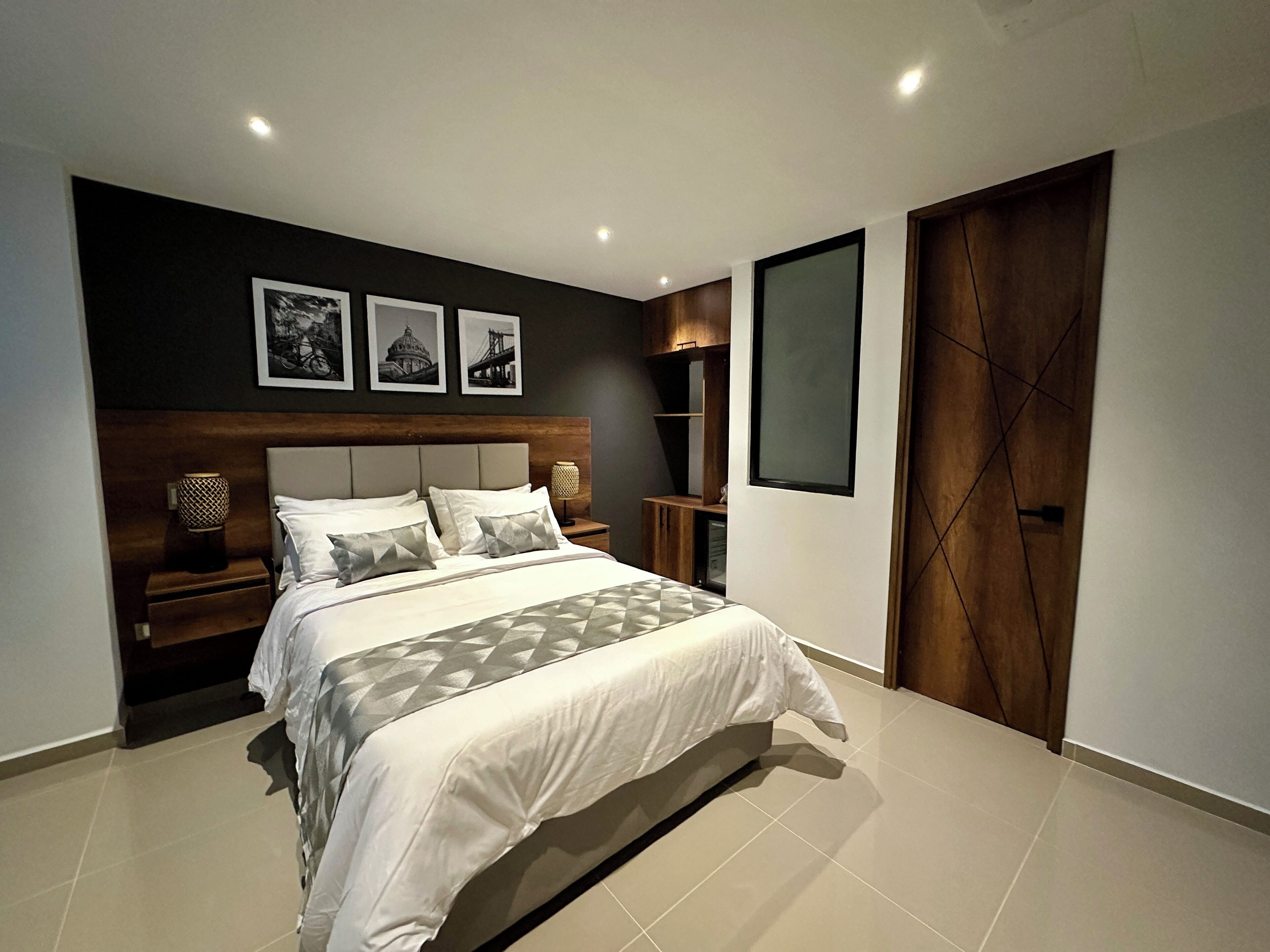 A modern bedroom with a large bed, a wooden headboard, and a nightstand with a lamp.