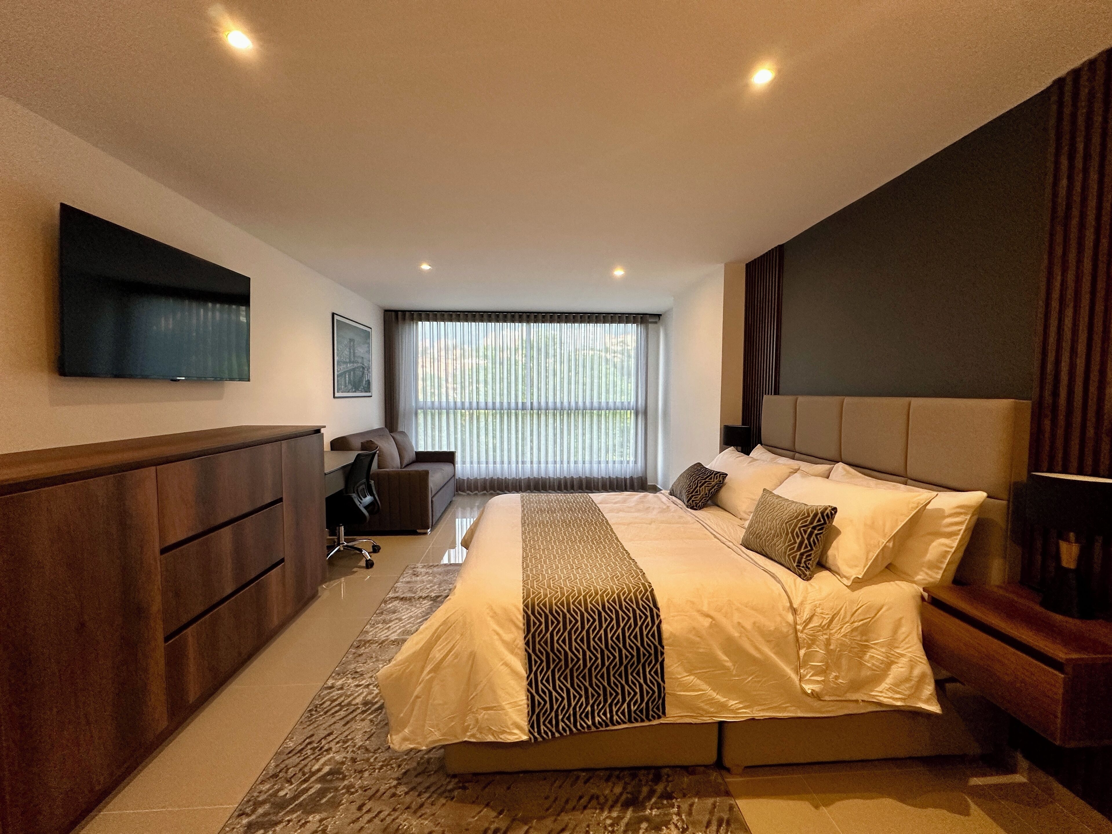 Een moderne hotelkamer met een groot bed, een bureau, een stoel, een televisie en een raam met gordijnen.