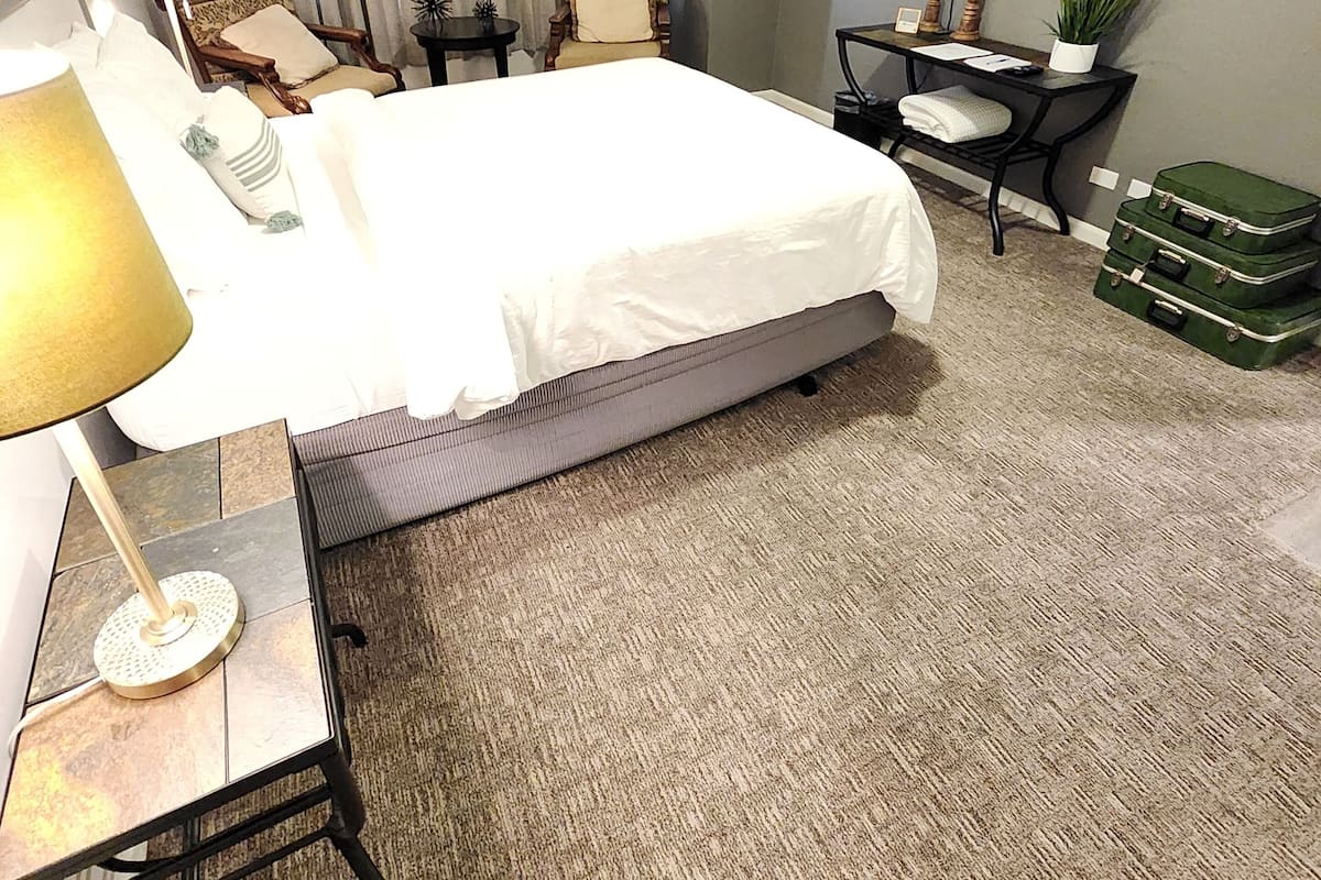 A hotel room with a bed, a desk with a lamp, a chair, a television on the wall, and a small table with a plant.