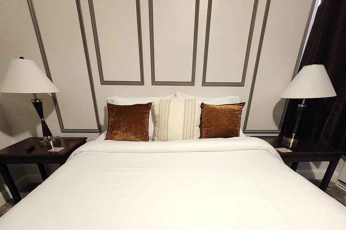 A neatly made bed with white bedding and two brown pillows, flanked by nightstands with lamps.