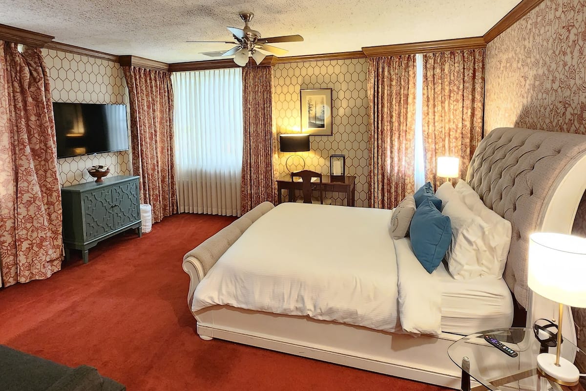 A hotel room with a large bed, a desk, a television, and a ceiling fan.
