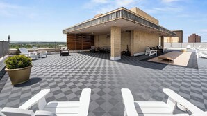 Una terraza en la azotea con piso a cuadros, mobiliario exterior y una zona cubierta con fachada de ladrillo.