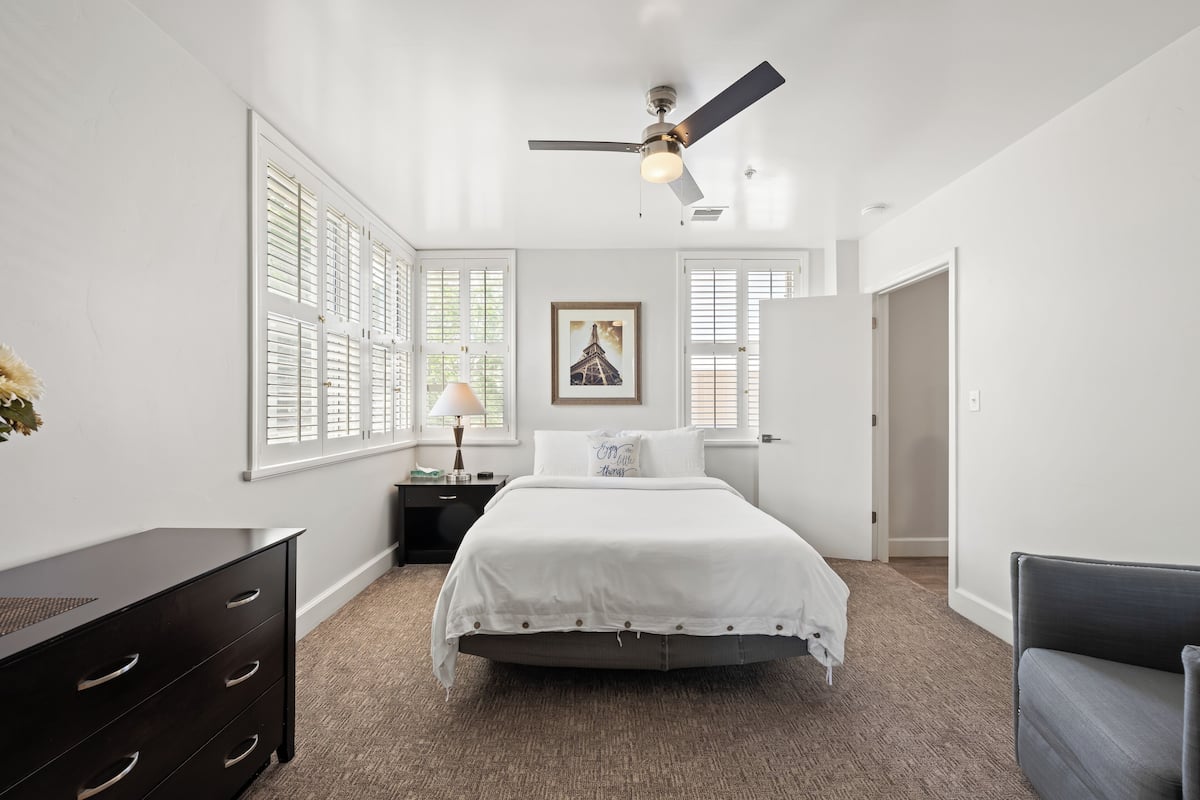 A bedroom with a bed, a nightstand, a dresser, and a ceiling fan.
