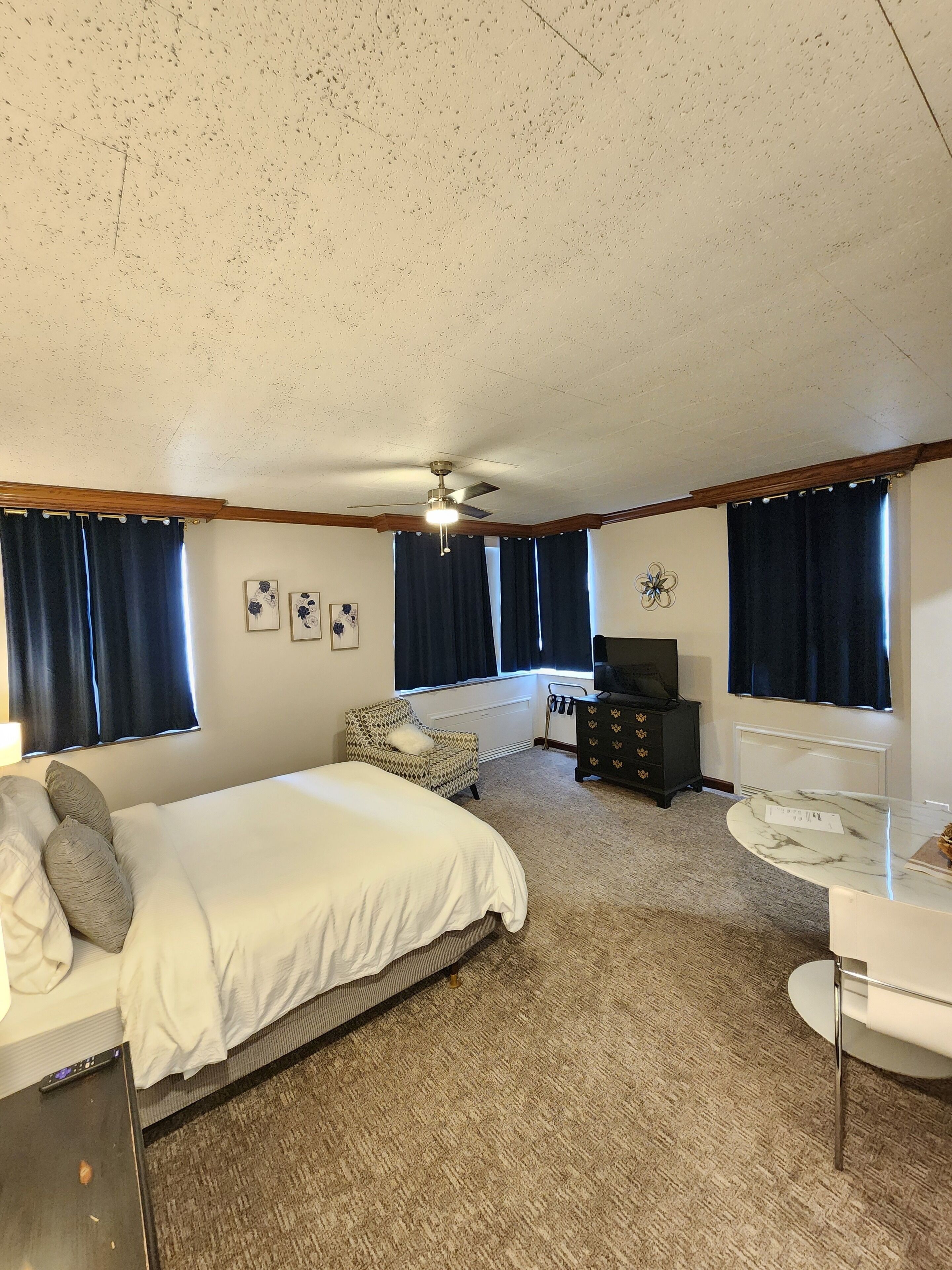 A bedroom with a bed, a desk, a chair, a dresser, and a ceiling fan.