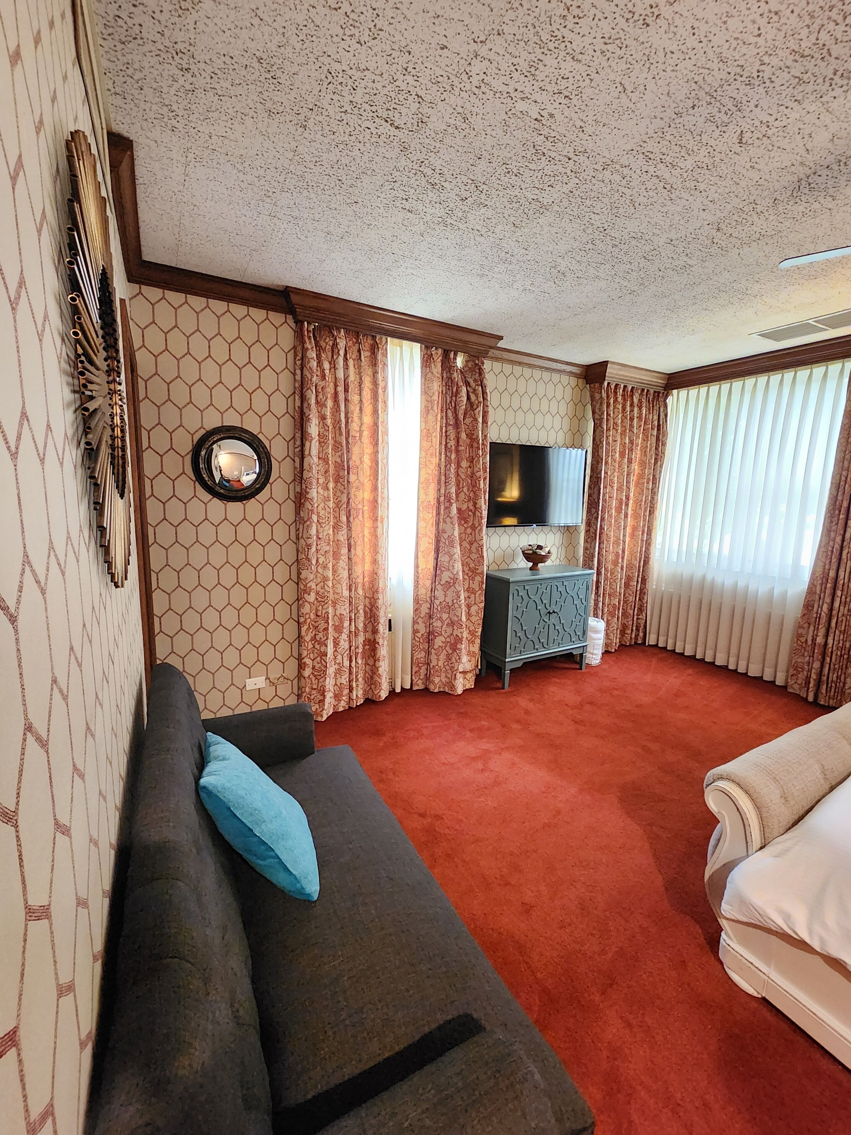 A hotel room with a sofa, a bed, a TV, a small table, and a mirror.