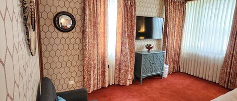 A hotel room with a sofa, a bed, a TV, a small table, and a mirror.