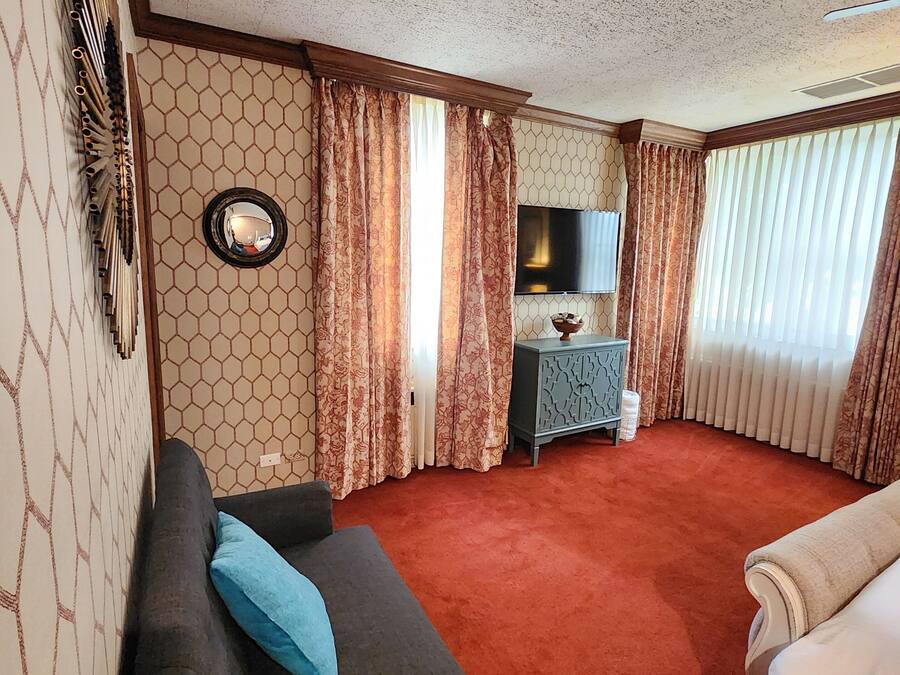 Una habitación de hotel con sofá, cama, televisión, una mesita y espejo.