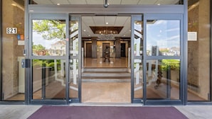 Entrada de un hotel con puerta de vidrio, piso de mármol y una escalera que conduce al interior.