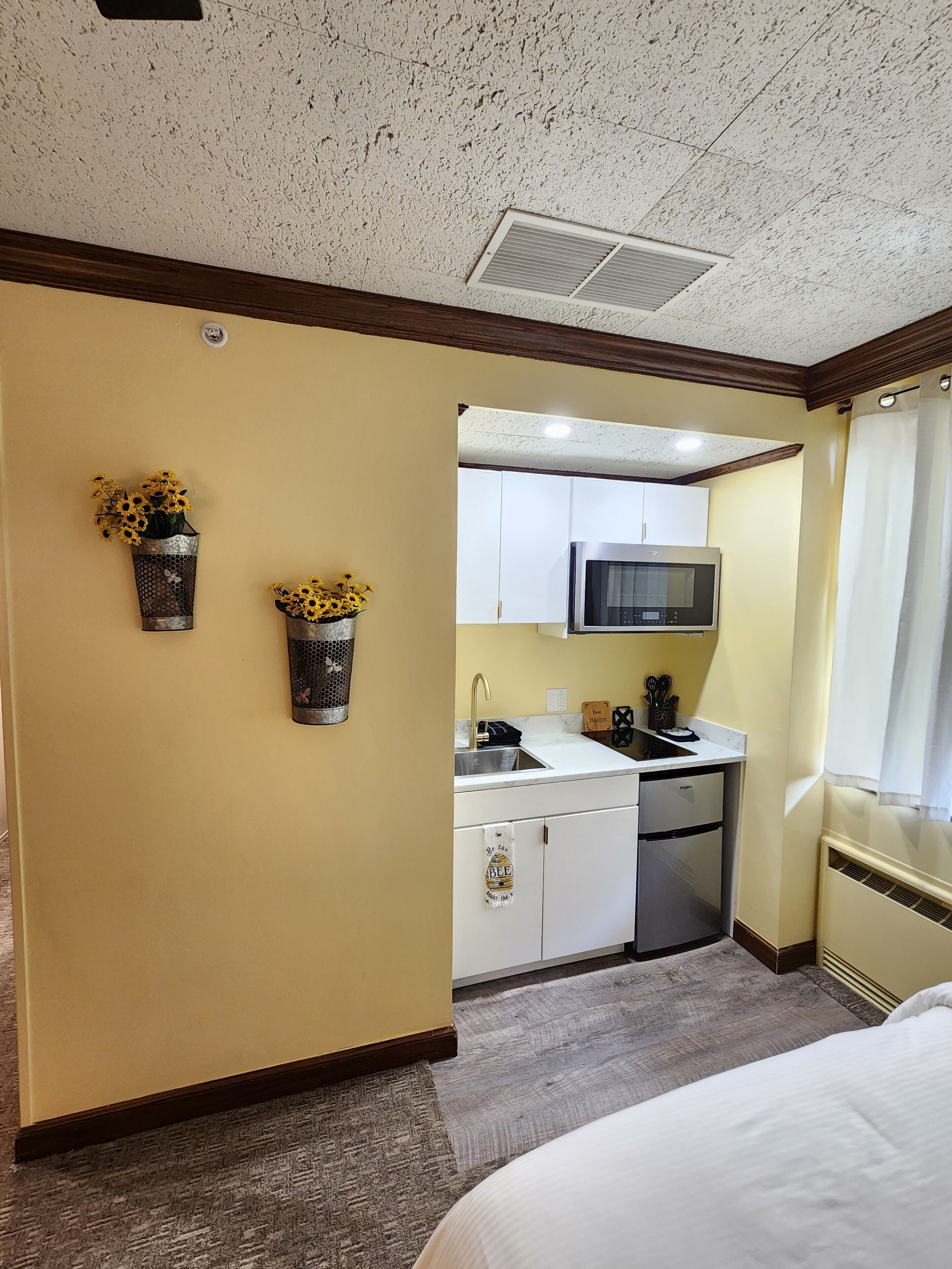 Una habitación de hotel con kitchenette, una cama y dos jarrones de flores colgados en la pared.