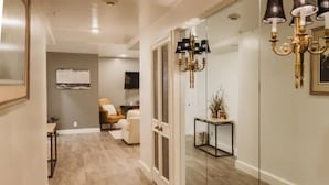 A hallway with a wooden floor, a glass door, a seating area with a chair and a small table, and a wall-mounted lamp. - Hotel Phillips (Bartlesville)