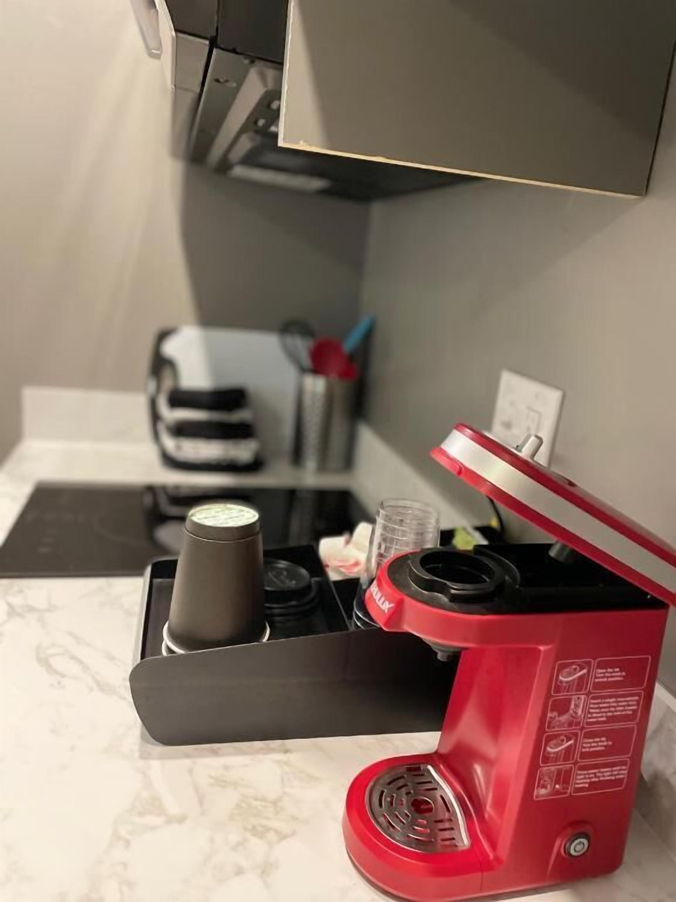 Una macchina da caffè rossa su un piano di lavoro in marmo, con una macchina per il caffè bianco e nero sullo sfondo.