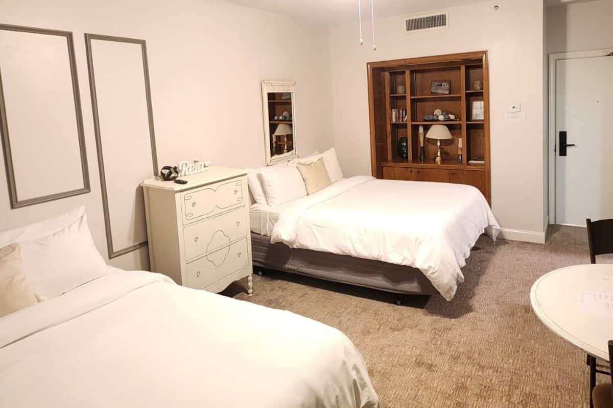 A bedroom with two beds, a dresser, a wooden cabinet, and a small table.