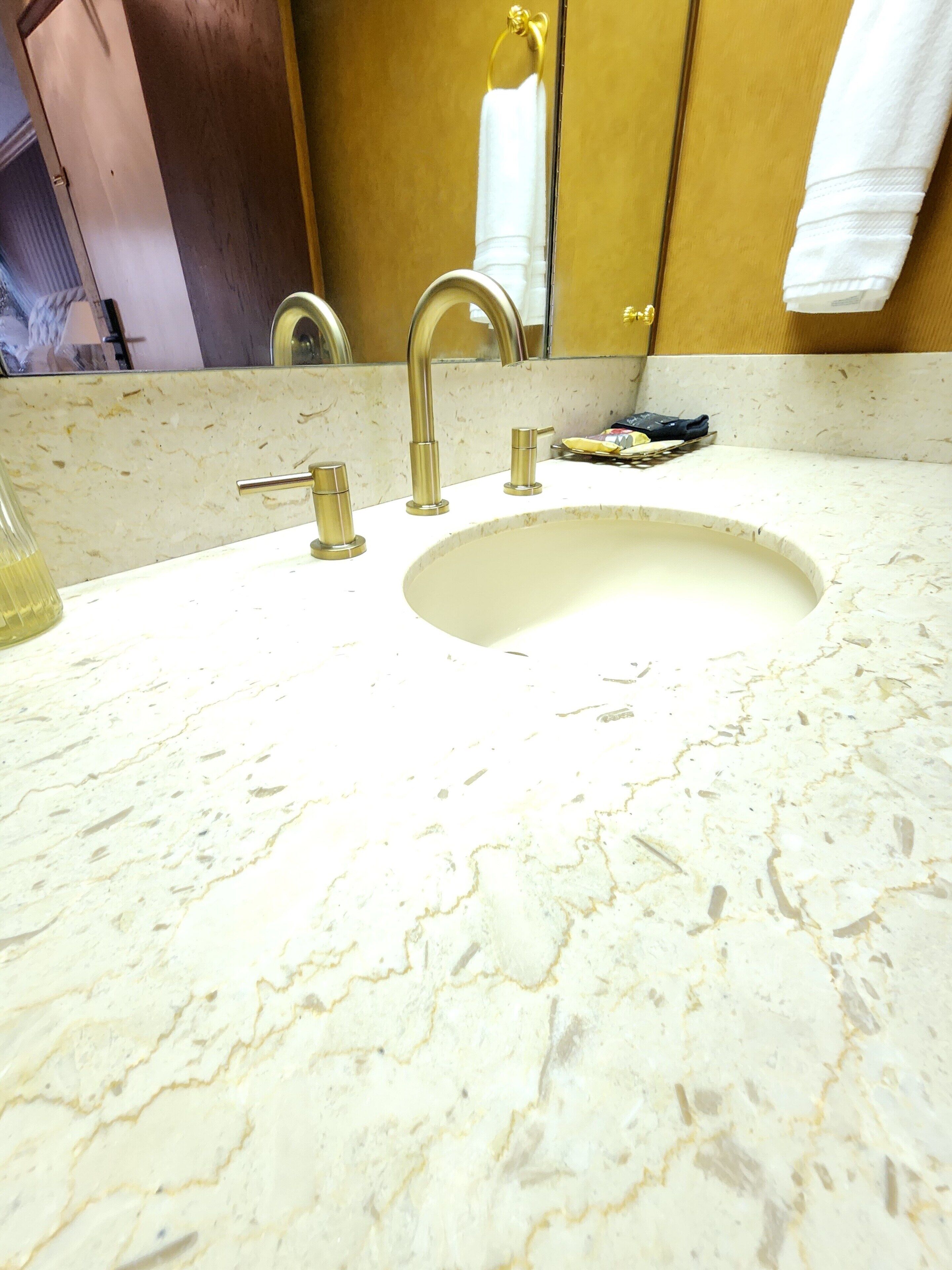 A bathroom with a marble sink, gold faucets, and a mirror.
