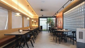 Un ristorante moderno con lunghi tavoli comuni, sedie nere e un'ampia parete vetrata.