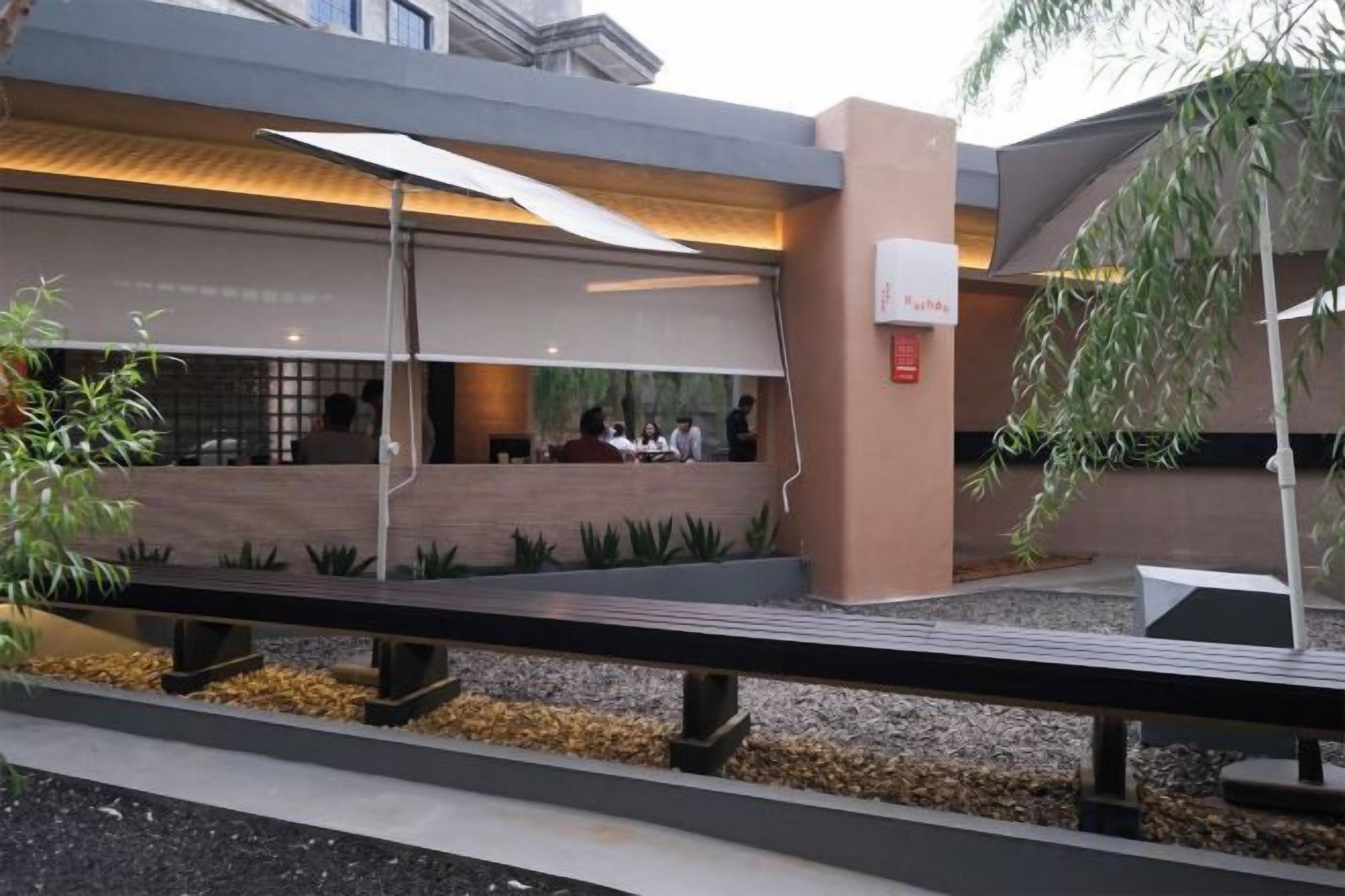 An outdoor seating area with tables and chairs, a covered walkway, and a building with a modern design.