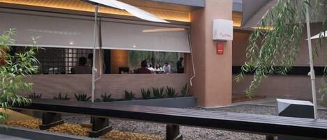 An outdoor seating area with tables and chairs, a covered walkway, and a building with a modern design.