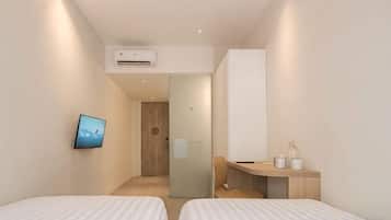 A modern hotel room with two beds, a TV, a desk, and a bathroom visible through a glass door.