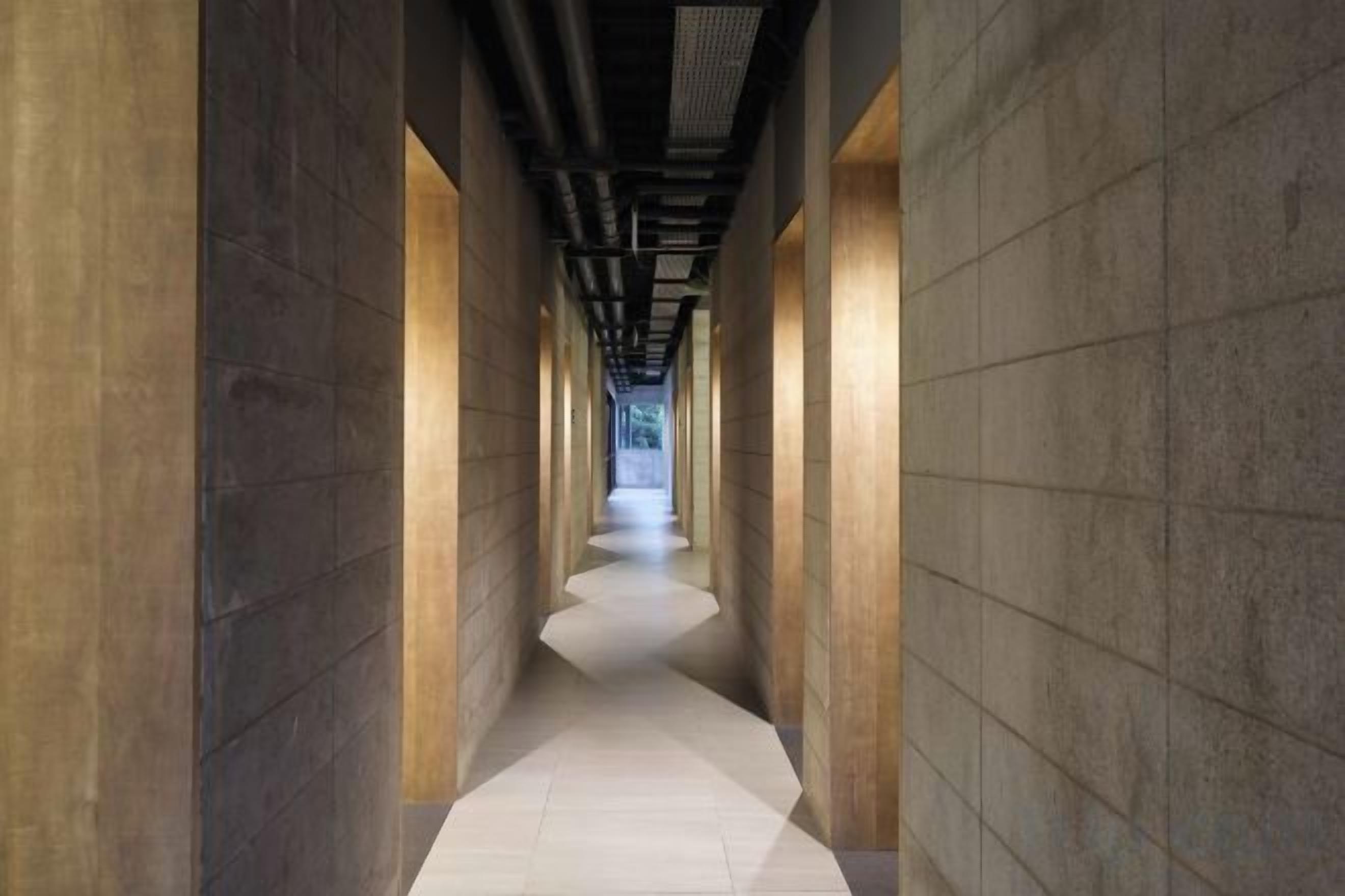 A corridor with a series of columns and a tiled floor, leading to a bright exit.