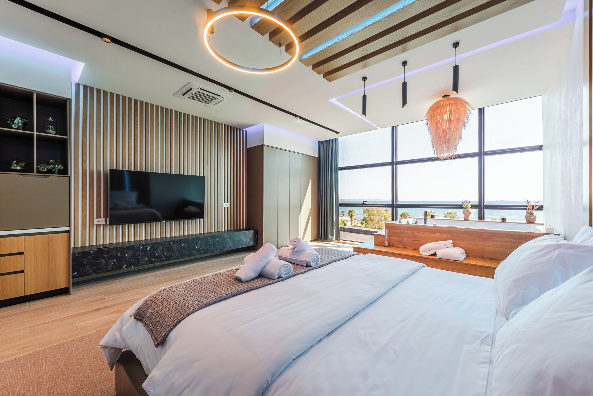 A modern bedroom with a large bed, a TV, and a view of the outdoors.