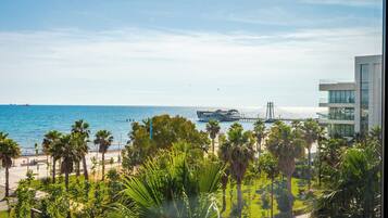 A coastal hotel with a view of the sea, palm trees, and a modern building with glass windows.