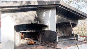 A wood-fired oven with a pizza inside, a chimney, and a metal rack. - Oasi Villa Anthea Apartment with Exclusive-Use Pool, Wi-Fi, and Air Conditioning (Monopoli)