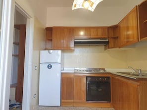 Eine kleine Küche mit Holzausstattung, einem weißen Kühlschrank, einem Herd und einem Backofen.