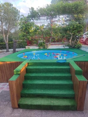 Une piscine avec des marches menant à l’intérieur, entourée de verdure et d’une clôture rouge.
