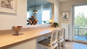 Una cucina moderna con un piano di lavoro in legno, sedie bianche, una ciotola, una lampada a sospensione e una finestra con tende.