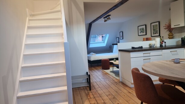 Een moderne keuken met een houten vloer, witte kasten en een eethoek met twee stoelen.