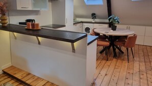 Een moderne keuken met witte kastjes, een houten aanrechtblad en een ingebouwde wasmachine. Er staat een ronde eettafel met stoelen en een kleine potplant.