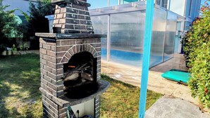 A brick-built outdoor oven with a chimney, a blue door, and a hose attached to the base. - Şilede doğa içinde denize yakın kapalı ısıtmalı havuzlu şömineli barbekülü villa (İmrenli)