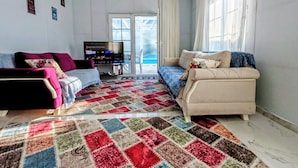 A living room with a large TV, two sofas, a patterned rug, and a sliding glass door leading to a balcony. - Şilede doğa içinde denize yakın kapalı ısıtmalı havuzlu şömineli barbekülü villa (İmrenli)