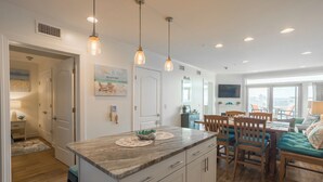 Una cocina moderna con una isla central, iluminación colgante y una zona de comedor con sillas y mesa de madera.
