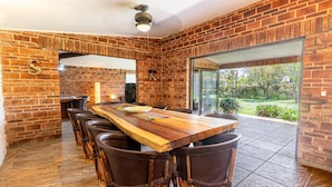 A spacious dining area with a long wooden table and multiple chairs, brick walls, and a large glass door leading to an outdoor garden. - Anana Casa SK Villa With Garden Family-friendl (Chapala)