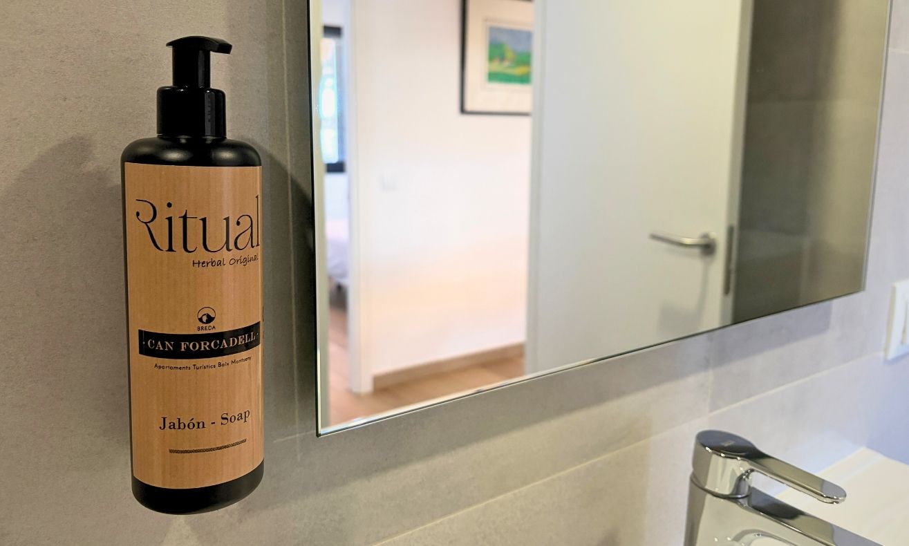 A bottle of Ritual Herbal Origins soap on a bathroom counter with a mirror reflecting a door and a hallway.